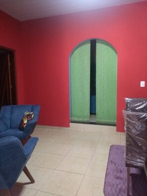 A room with a red wall, a blue chair, a green door, and a purple bench. - Casa super confortável (Anapolis)