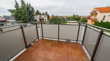 A balcony with a tiled floor, metal railing, and a view of surrounding buildings and trees.