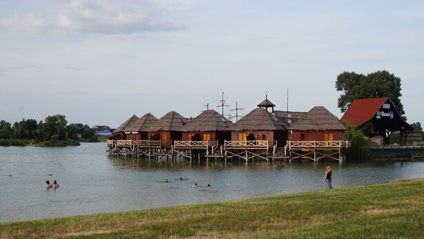A lakeside property with thatched-roof cottages on stilts, a dock, and a grassy area. - Apartment Dolfi (Senec)