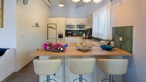 Eine Küche mit einer Holztheke, weißen Barhocker, einem Kühlschrank und einer Kaffeemaschine.