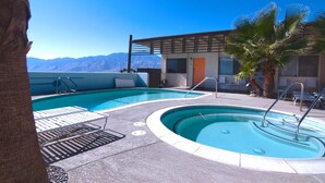 A pool area with lounge chairs and a palm tree, surrounded by mountains. - The Getaway Studio #3: Pool, Mountain View, Kids welcome (Desert Hot Springs)