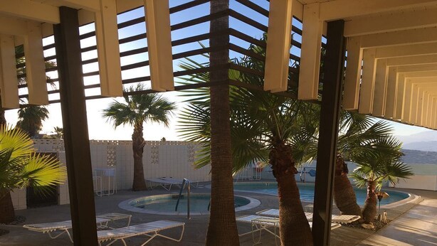 A covered outdoor area with palm trees, lounge chairs, and a pool. - The Getaway Studio #3: Pool, Mountain View, Kids welcome (Desert Hot Springs)