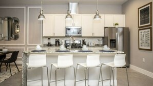 A modern kitchen with white cabinets, stainless steel appliances, and bar stools.
