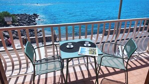 A balcony with two chairs and a table, overlooking a rocky coastline and the sea.