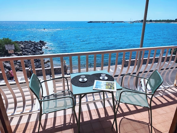A balcony with two chairs and a table, overlooking a rocky coastline and the sea.