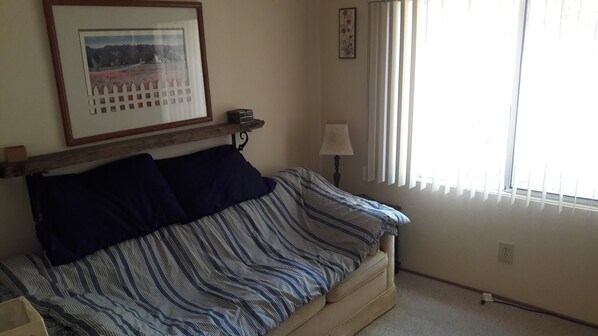 A room with a bed, a framed picture on the wall, a lamp, and a window with blinds.