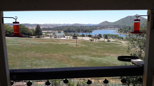A view from a window overlooking a grassy field, a lake, and distant mountains.