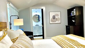 A hotel room with a large bed, a desk, a chair, a lamp, a mirror, a microwave, and a framed artwork on the wall. - Private cottage located on The Carriage House Inn Estate (Mena)