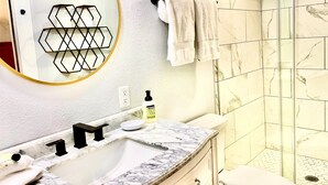 A bathroom with a marble sink, a round mirror, a towel rack, and a shower with hexagonal tiles. - Private cottage located on The Carriage House Inn Estate (Mena)