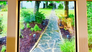 A view through a window with a stone pathway leading to a garden area. - Private cottage located on The Carriage House Inn Estate (Mena)