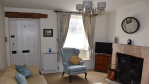A living room with a sofa, armchair, fireplace, and a television. - Period cottage in idyllic riverside location in prime Cotswolds village (Lower Slaughter)