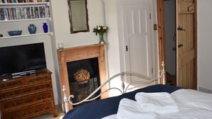 A bedroom with a bed, a television on a dresser, a bookshelf, a mirror, and a wooden door. - Period cottage in idyllic riverside location in prime Cotswolds village (Lower Slaughter)
