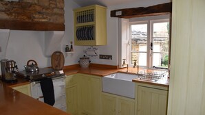 A kitchen with yellow cabinets, a wooden countertop, a built-in sink, and a window with a view of the outside. - Period cottage in idyllic riverside location in prime Cotswolds village (Lower Slaughter)