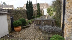 A stone building with a white door, a wooden bench, and a potted plant. - Period cottage in idyllic riverside location in prime Cotswolds village (Lower Slaughter)