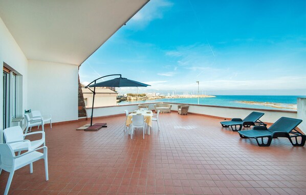 A terrace with a table set for dining, lounge chairs, and a view of the sea. - 2 bedroom awesome apartment in Porto Torres (Porto Torres)