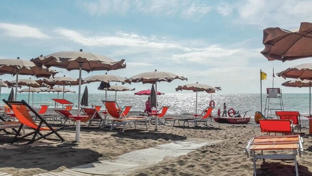 Een strand met rijen ligbedden en parasols, een reddingsboei en een boot in het water.