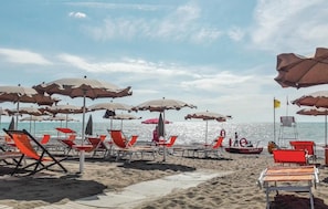 A beach with rows of sun loungers and umbrellas, a lifebuoy, and a boat in the water. - Amazing home in Sassetta with WiFi (Sassetta)