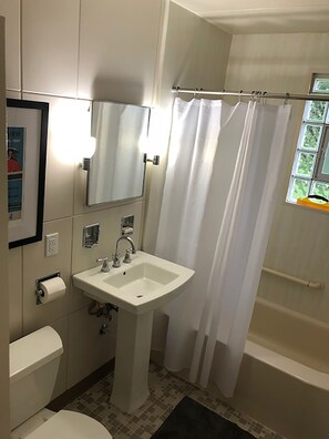 Une salle de bain avec un lavabo blanc, des toilettes, un miroir et un rideau de douche.