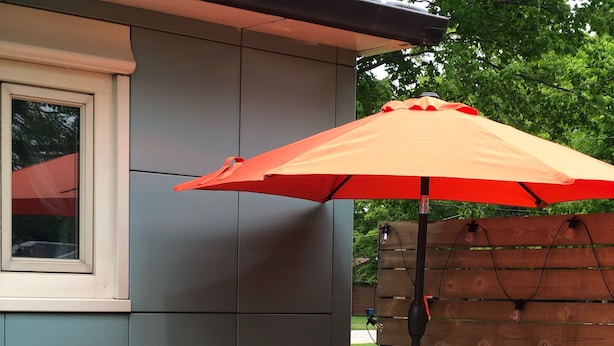 A patio with a wooden table, two wicker chairs, a sofa with orange cushions, and a large orange umbrella. - Blue Steel Lustron - Rare - Near Starved Rock Country (Grand Ridge)