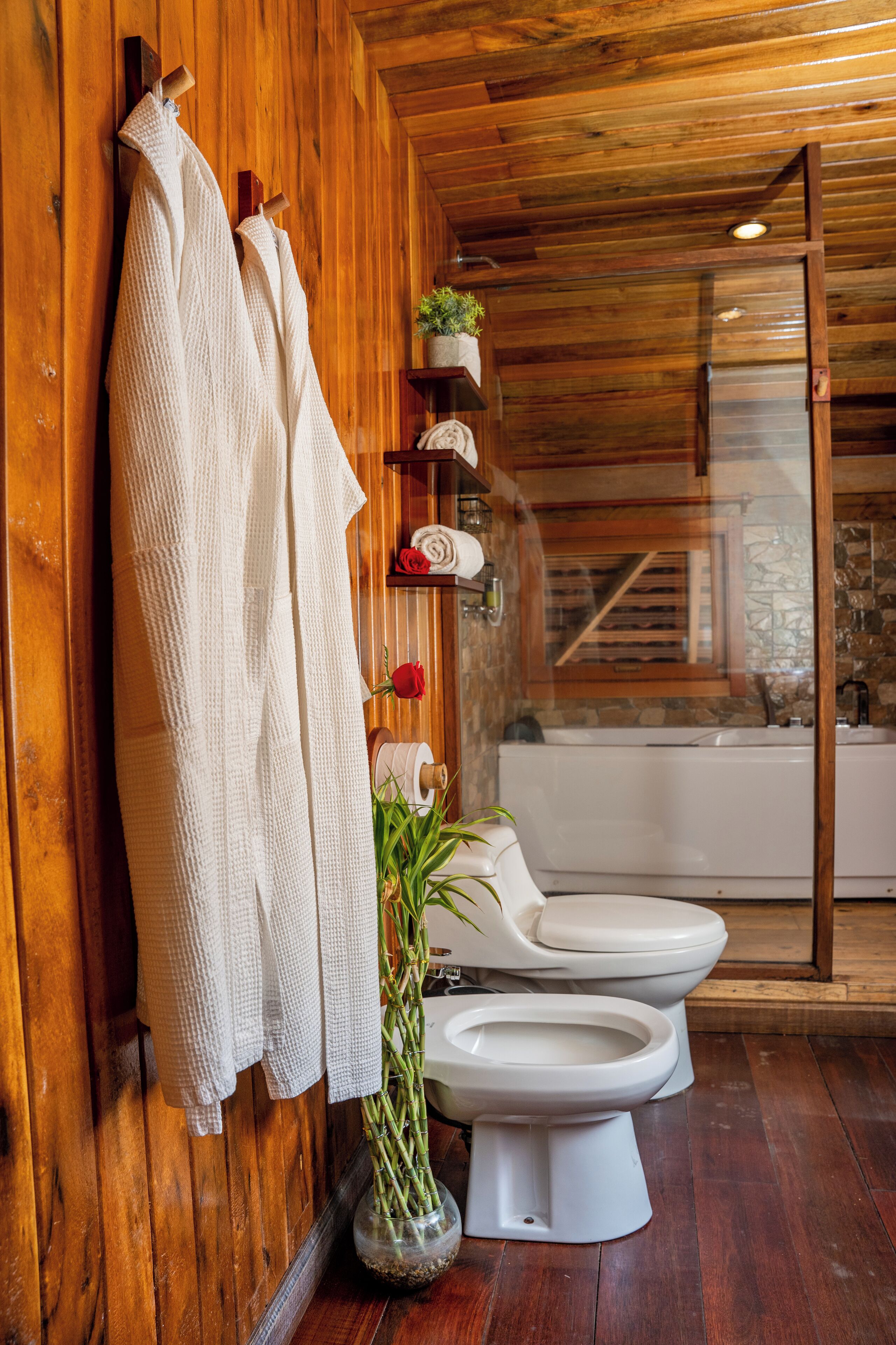 Un baño de madera con dos inodoros, una ducha y una planta.