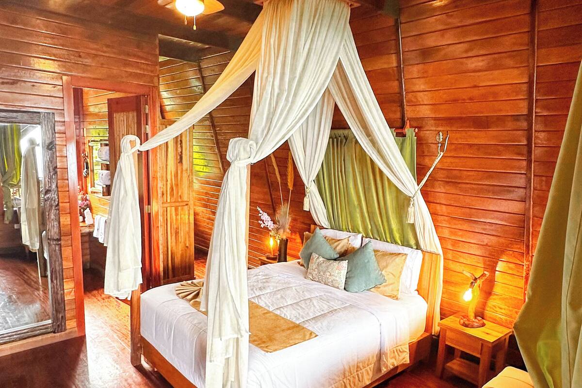A wooden cabin bedroom with a canopy bed, a sofa, and a small table with a lamp.