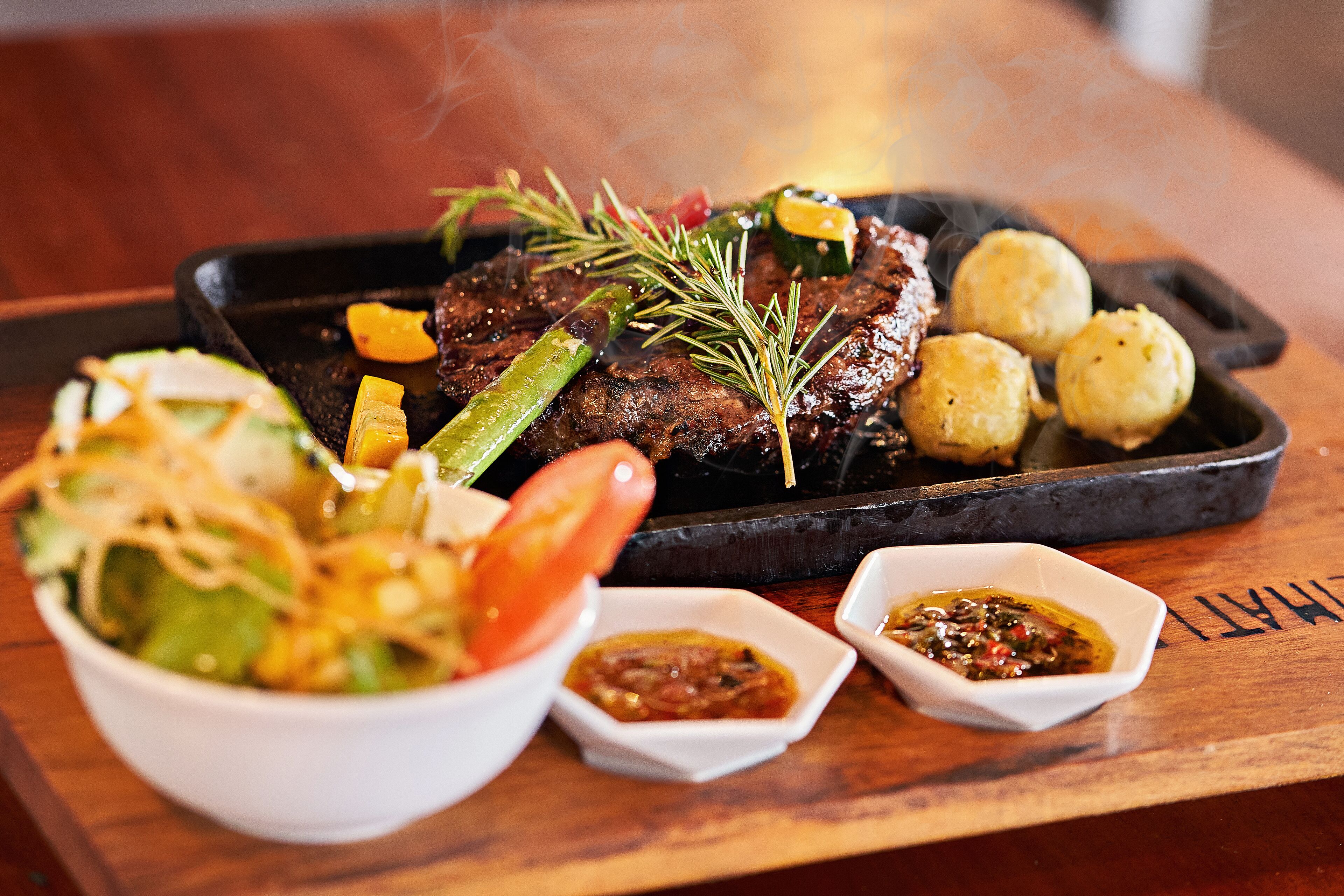 Un repas composé d’un steak, de légumes et de deux petits ramequins de sauce, le tout servi sur une table en bois.