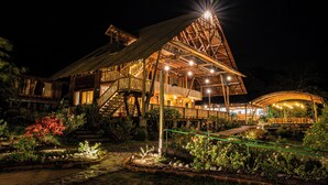 A large wooden house with multiple levels and a covered outdoor area, surrounded by well-maintained gardens.