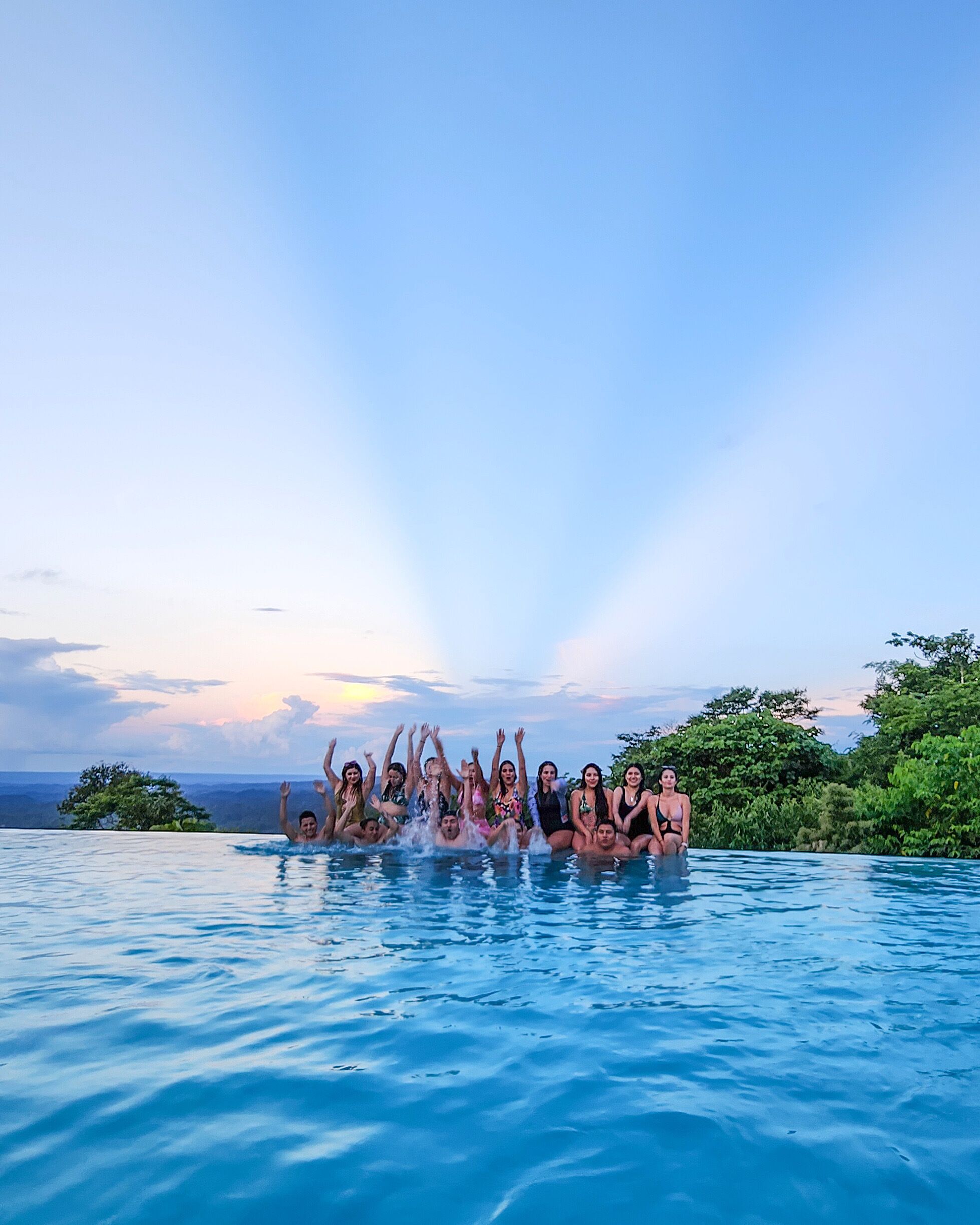 A group of people in a swimming pool with a scenic view of the ocean and hills in the background.