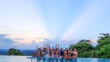 A group of people in a swimming pool with a scenic view of the ocean and hills in the background.