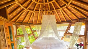 A circular bed with a canopy in a room with a wooden ceiling and large windows.