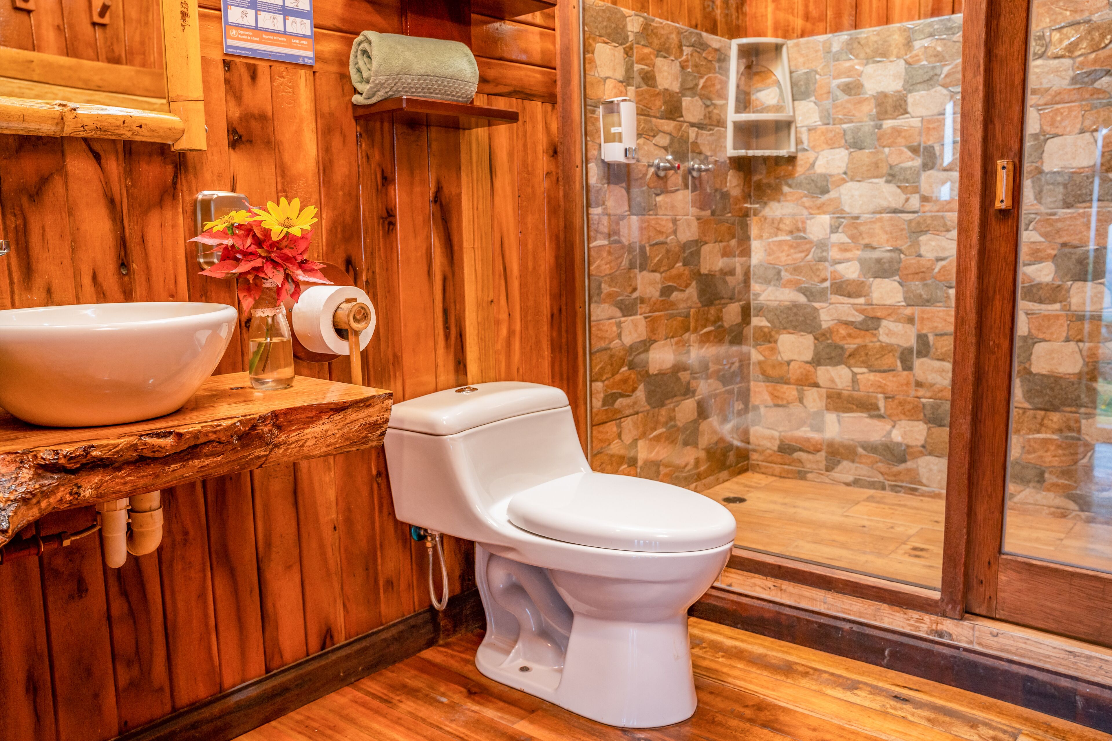 Une salle de bain en bois avec un mur de douche en pierre, un lavabo blanc et des toilettes.