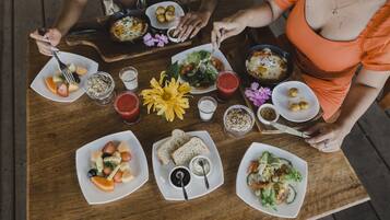Een houten tafel met diverse gerechten, zoals fruit, brood en salades, klaar voor een maaltijd.