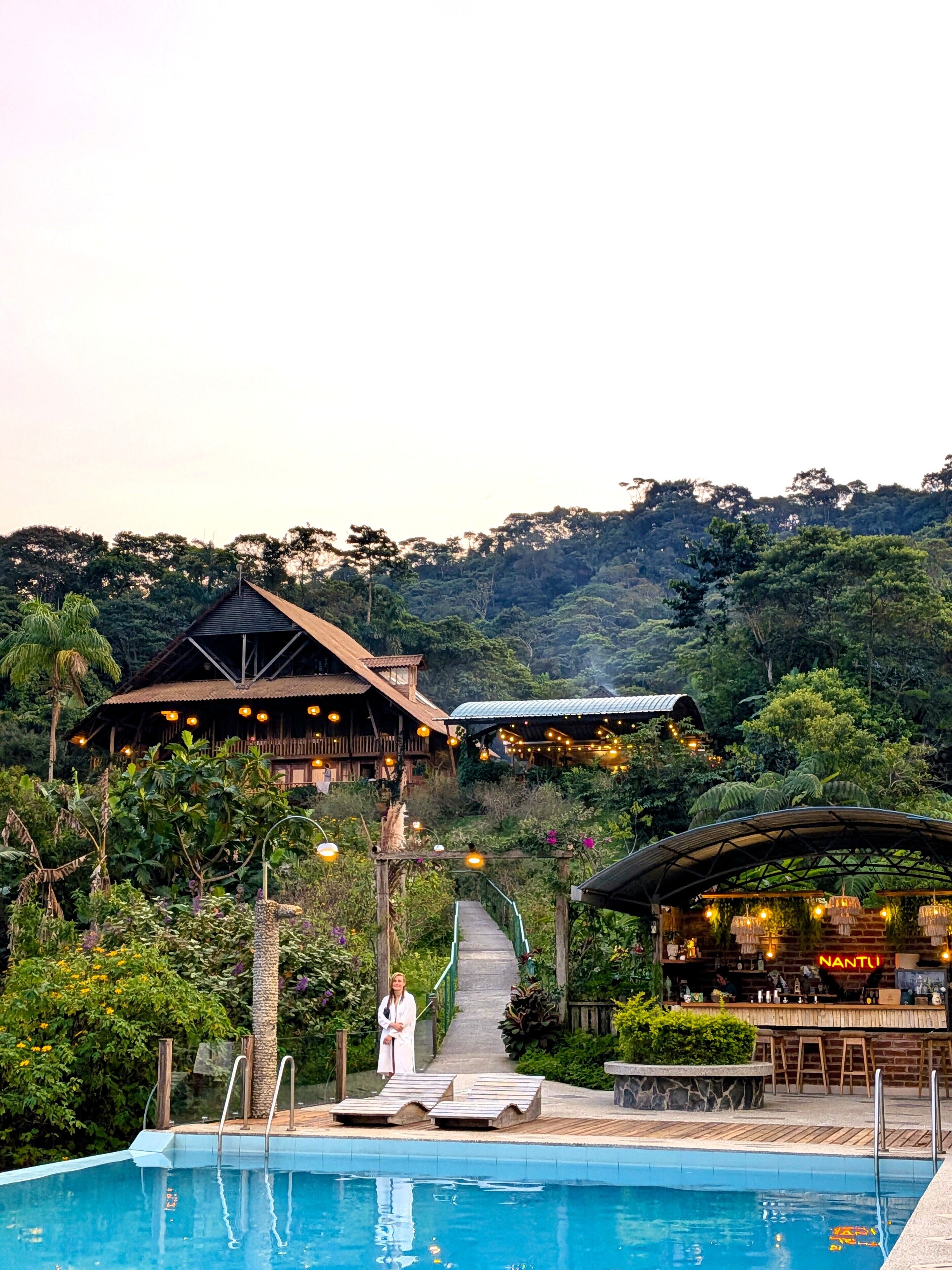 A pool area with lounge chairs, a bar, and a pathway leading to a building with a thatched roof.