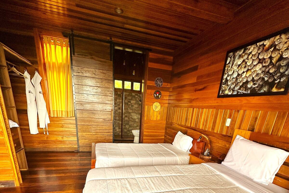 A wooden room with a large bed, a shower, and a wooden ceiling.