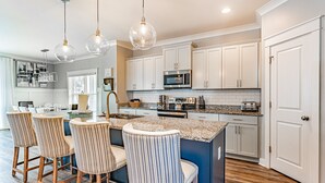 A modern kitchen with white cabinets, a central island with bar stools, and a microwave.