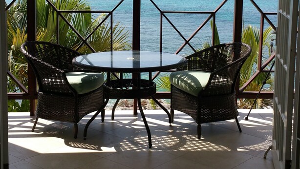 A balcony with two wicker chairs and a table, overlooking the ocean. - Beachfront - Relaxing views (Speightstown)