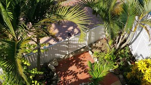 A courtyard with a paved walkway, surrounded by various plants and a white fence. - Beachfront - Relaxing views (Speightstown)