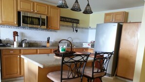 A kitchen with wooden cabinets, a stainless steel refrigerator, a microwave, and a sink. There are two bar stools with cushioned seats. - Beachfront - Relaxing views (Speightstown)