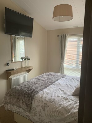 Una camera da letto con un letto, una TV a parete, un termosifone, uno scaffale con un cartello che dice 'Love' e una finestra con tende.