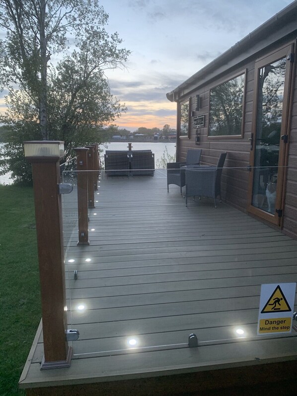 Un terrazzo in legno con mobili da esterno, un segnale di avvertimento e vista su un lago.