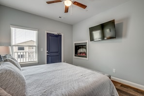 Ein Schlafzimmer mit einem Bett, einem Deckenventilator, einem an der Wand befestigten Fernseher und einem Fenster mit Jalousien.