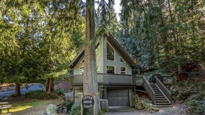 A lodge with a wooden exterior, a covered porch, and a staircase leading to a garage. - Cedar Grove Lodge | BBQ | Wifi, Hot tub, AC (Packwood)