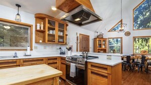 A kitchen with wooden cabinets, a large island, and a dining area with chairs. - Cedar Grove Lodge | BBQ | Wifi, Hot tub, AC (Packwood)