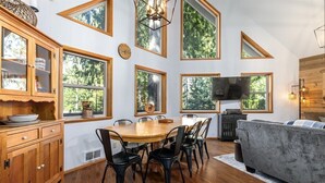 A dining area with a wooden table and chairs, a sofa, and a television. - Cedar Grove Lodge | BBQ | Wifi, Hot tub, AC (Packwood)