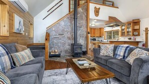 A cozy living room with a stone fireplace, grey sofas, and a wooden coffee table. - Cedar Grove Lodge | BBQ | Wifi, Hot tub, AC (Packwood)