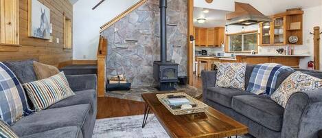 A cozy living room with a stone fireplace, grey sofas, and a wooden coffee table.