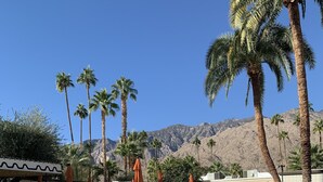 Ein Poolbereich mit Liegestühlen und Sonnenschirmen, Palmen und einem Berg im Hintergrund.