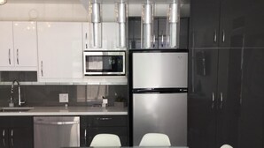 Eine moderne Küche mit Esstisch aus Glas, weißen Stühlen, Edelstahlgeräten und dunklen Schränken.