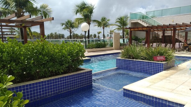 Zona de piscina con suelo azulado de baldosas, rodeada de vegetación y palmeras.