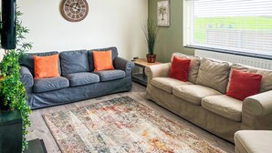 A living room with two sofas, a coffee table, a potted plant, a wall clock, and a window with blinds. - 4 bedroom accommodation in Criccieth, near Porthmadog (Criccieth, near Porthmadog)